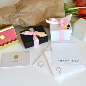 May include: A white box with a pink ribbon and the text "FONDEUR" on the front. The box is sitting on a white surface next to a thank you card with the text "THANK YOU www.FONDEUR.etsy.com".