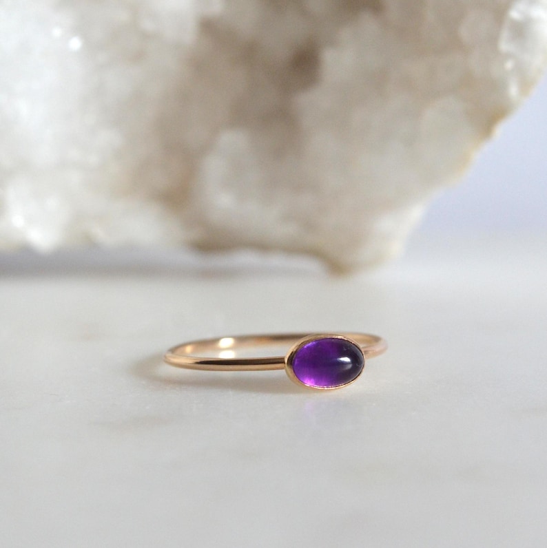 May include: A delicate gold ring with a purple amethyst gemstone. The ring is simple and elegant, perfect for everyday wear.