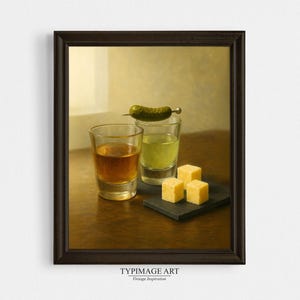 May include: A framed print depicting a still life with two shot glasses, one with a golden liquid and the other with a green liquid. A gherkin on a cocktail stick and three yellow cheese cubes are also present.