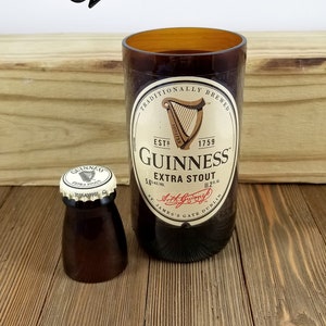 May include: A brown glass bottle with a label that reads "Traditionally Brewed" and "Guinness Extra Stout". The bottle is sitting on a wooden surface next to a smaller brown glass bottle with a cap that reads "Guinness Extra Stout".