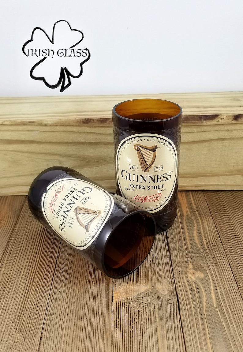 May include: Two brown glass Guinness beer bottles repurposed into drinking glasses. The bottles have the Guinness logo and text, "Traditionally Brewed", "Est. 1759", "Extra Stout", and "Arthur Guinness, Dublin".