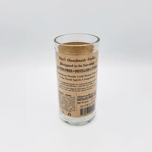 May include: A clear glass tumbler repurposed from a Tito's Handmade Vodka bottle. The label features black text on a tan background, stating Tito's Handmade Vodka, Gluten-Free, Distilled 6 Times, 80 Proof, and 375 ml. A shamrock logo reads Irish Glass.
