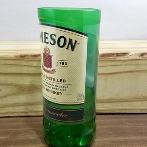 May include: A green glass shot glass with a Jameson Irish Whiskey label. The label features the Jameson logo, the year 1780, and the text "Triple Distilled Irish Whiskey Made the Jameson Way Since 1780".