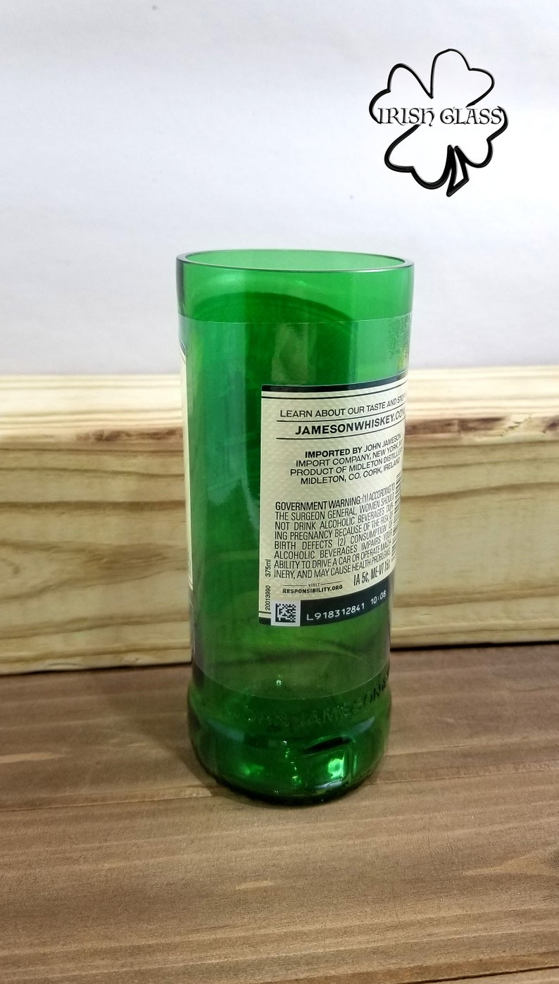 May include: A green glass bottle with a label that reads "LEARN ABOUT OUR TASTE AND STYLE" and "JAMESONWHISKEY.CO". The label also includes information about the importer, product, and government warnings. The bottle is sitting on a wooden surface.