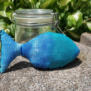 May include: A blue and green fabric fish toy with a grid pattern. The fish is lying on a gray surface.