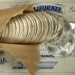 Puede incluir: Una pila de monedas de plata envueltas en papel marr&oacute;n, con el texto "CALIFORNIA" y "Gold Dust" visible en un documento antiguo.