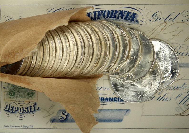 Puede incluir: Una pila de monedas de plata envueltas en papel marr&oacute;n, con el texto "CALIFORNIA" y "Gold Dust" visible en un documento antiguo.