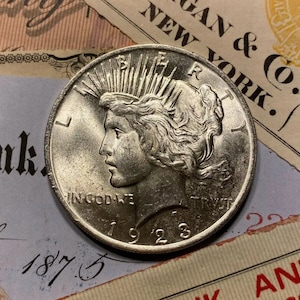 Puede incluir: Una moneda de plata Peace dollar con el a&ntilde;o 1923 inscrito en la parte inferior. La moneda presenta un perfil de una mujer con el pelo suelto y una corona de rayos. La inscripci&oacute;n "IN GOD WE TRUST" es visible por encima del a&ntilde;o.