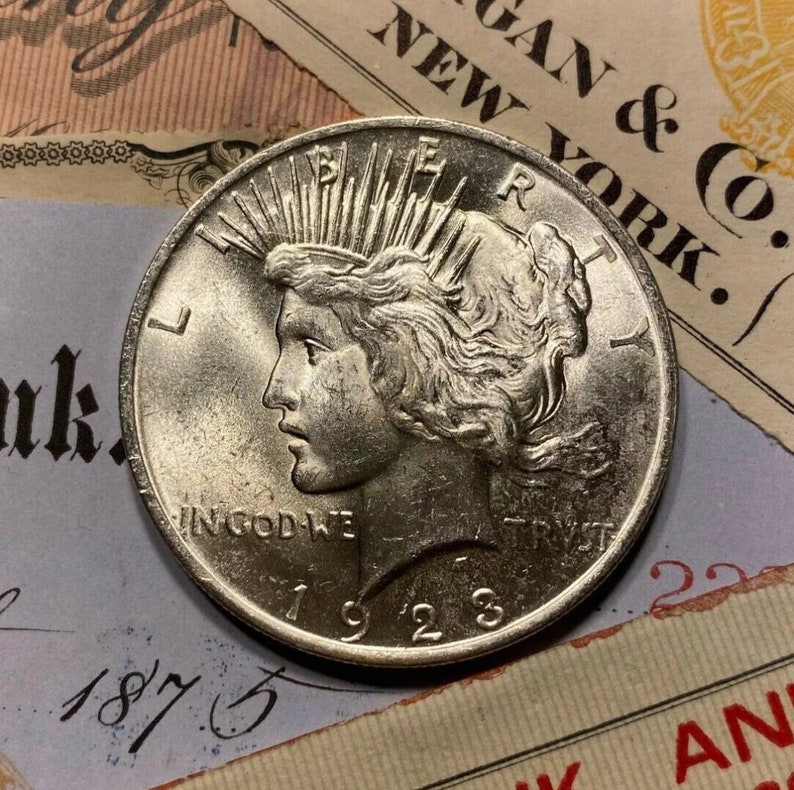 Puede incluir: Una moneda de plata Peace dollar con el a&ntilde;o 1923 inscrito en la parte inferior. La moneda presenta un perfil de una mujer con el pelo suelto y una corona de rayos. La inscripci&oacute;n "IN GOD WE TRUST" es visible por encima del a&ntilde;o.
