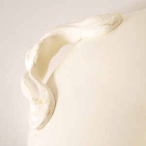 May include: White ceramic serving dish with a decorative, twisted handle. The handle is attached to the side of the dish.