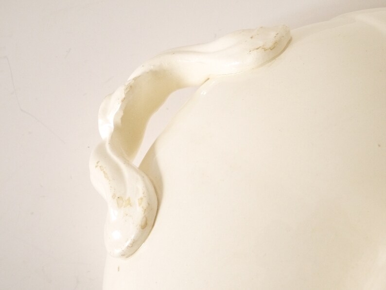 May include: White ceramic serving dish with a decorative, twisted handle. The handle is attached to the side of the dish.