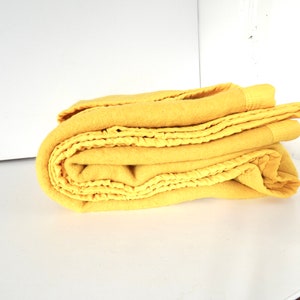 Puede incluir: Una manta de franela amarilla doblada cuidadosamente sobre una superficie blanca. La manta tiene una textura suave y peluda y está hecha de un material cálido y cómodo.