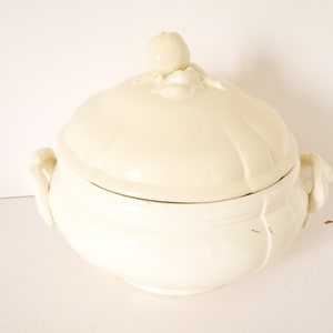 May include: White ceramic serving bowl with a lid. The bowl has two handles and the lid has a decorative knob.