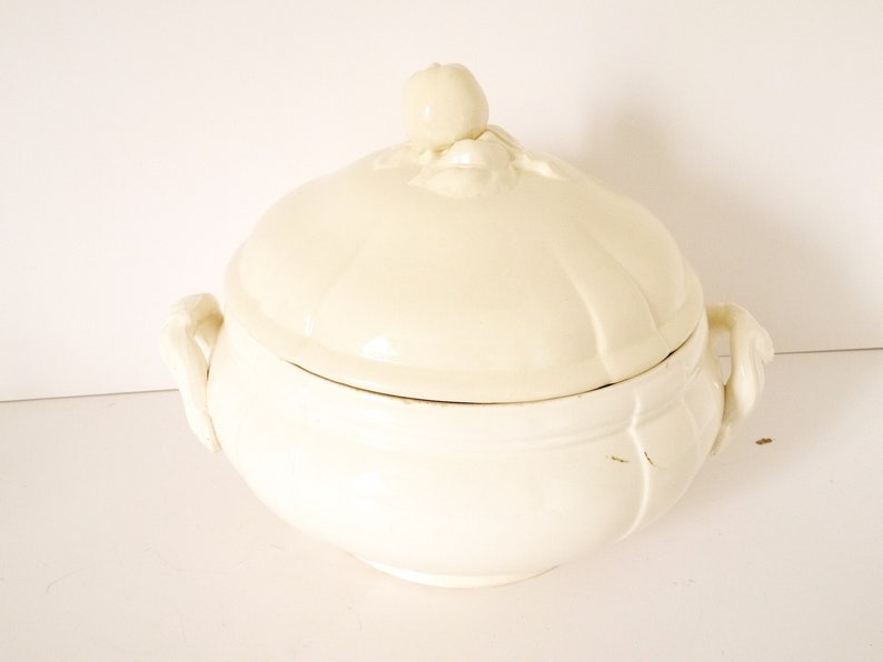 May include: White ceramic serving bowl with a lid. The bowl has two handles and the lid has a decorative knob.