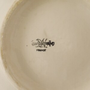 May include: Close-up of the bottom of a white ceramic plate with the text "Que du Bonheur" and "France" printed in black.