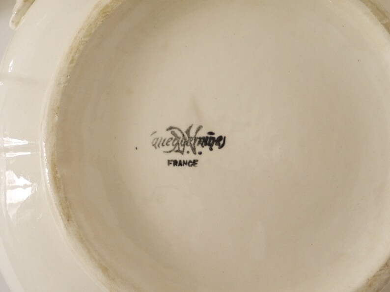 May include: Close-up of the bottom of a white ceramic plate with the text "Que du Bonheur" and "France" printed in black.