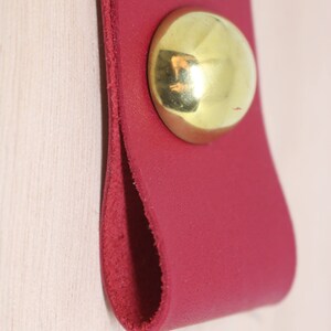 May include: A red leather pull handle with a brass knob. The handle is designed to be used on a drawer or cabinet door.