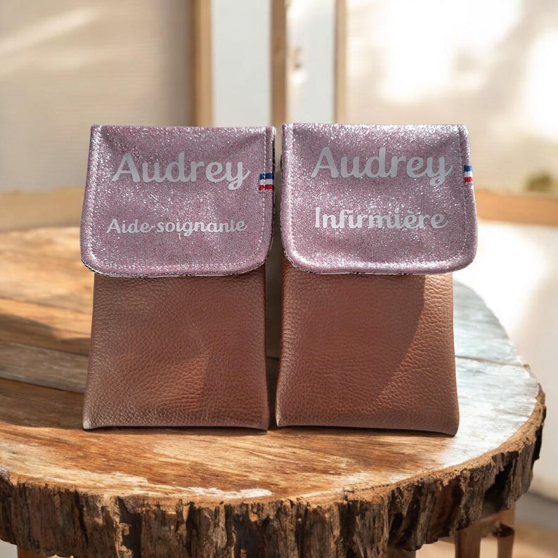 May include: Two small, brown pouches with glittery pink flaps. Each flap is personalized with the name "Audrey" and a French flag design. One pouch reads "Aide-soignante" and the other reads "Infirmi&egrave;re".