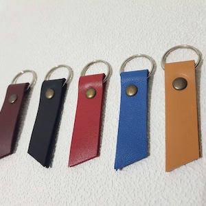 Puede incluir: Cinco llaveros de cuero con anillos de metal. Los llaveros son de diferentes colores: rojo, azul, negro, marrón y beige.