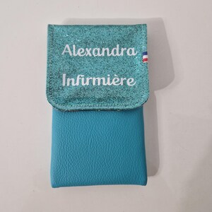 May include: A turquoise blue pouch with a glittery flap. The flap has the name "Alexandra" and the word "Infirmi&egrave;re" printed in white. A small French flag is on the right side of the flap.