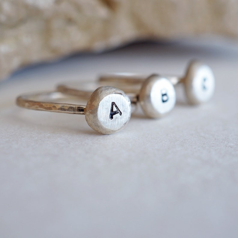 May include: Three silver rings with hammered bands and round tops. Each ring has a different letter engraved on the top: A, B, and C.