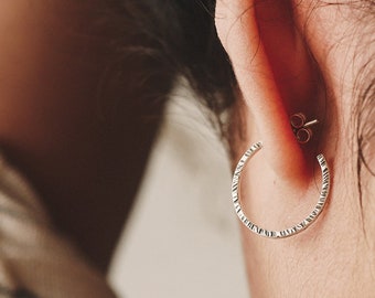 May include: A close-up of a person's ear wearing a silver hoop earring with a textured surface.