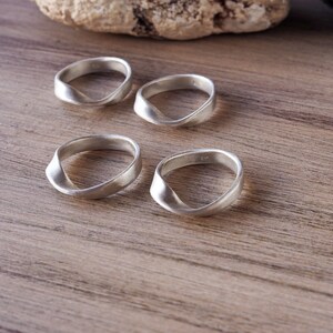 Peut inclure: Quatre bagues en argent au design torsadé sont présentées sur une surface en bois. Les bagues ont une finition mate et une esthétique simple et moderne. Les bagues sont probablement en argent sterling.