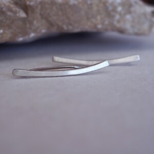 May include: A pair of silver ear cuff earrings. The earrings are curved and have a brushed finish.