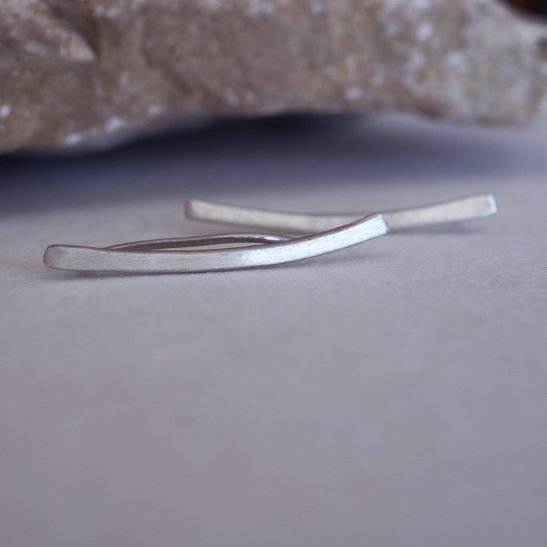 May include: A pair of silver ear cuff earrings. The earrings are curved and have a brushed finish.