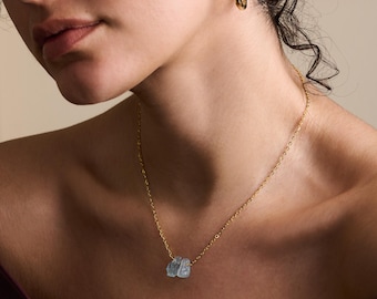 May include: A gold chain necklace with a light blue gemstone pendant. The pendant is made of two pieces of gemstone that are connected together.