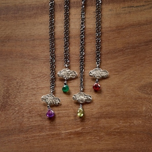 May include: Four silver necklaces with cloud charms and gemstone drops. The gemstones are green, red, purple, and yellow.