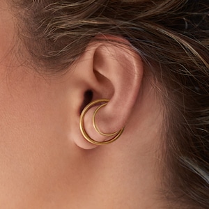 May include: A close-up of a person's ear with two gold hoop earrings. The earrings are stacked on top of each other, with the larger hoop on the outside and the smaller hoop on the inside.