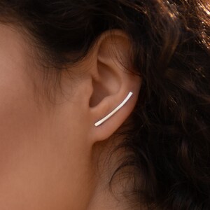 May include: A silver ear cuff with a curved bar design. The cuff is worn on the upper part of the ear.