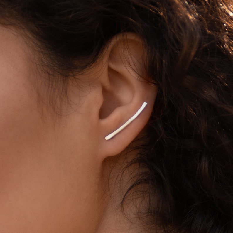 May include: A silver ear cuff with a curved bar design. The cuff is worn on the upper part of the ear.