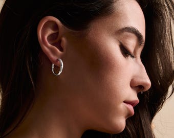 May include: A close-up of a person's ear with a silver hoop earring. The earring is simple and elegant, with a smooth, polished finish.