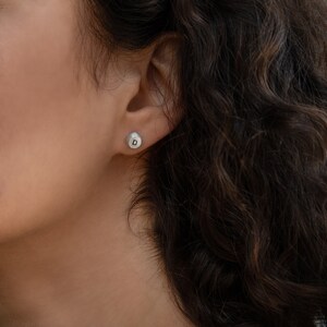 May include: A close-up of a person's ear with a small silver earring with the letter "D" on it.