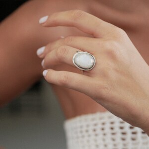 May include: A silver ring with a large oval moonstone set in a textured silver band.