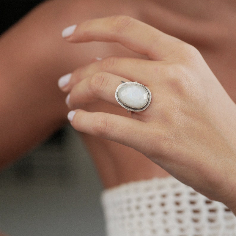 May include: A silver ring with a large oval moonstone set in a textured silver band.