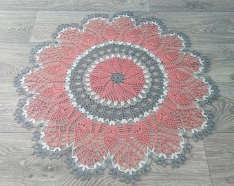 Puede incluir: Un encaje de ganchillo con un esquema de color rosa y gris. El encaje tiene una forma circular con un diseño central y múltiples capas de intrincado trabajo de ganchillo.