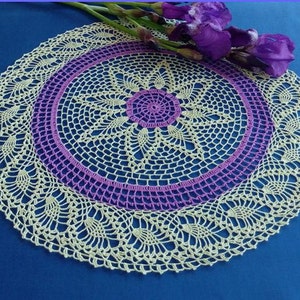May include: A crocheted doily with a delicate, lacy design. The doily is cream-colored with a purple center and a scalloped edge.
