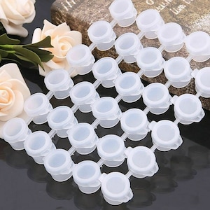 May include: A set of 24 small, clear plastic paint pots with lids, connected together in rows. The pots are arranged in a grid pattern and are ideal for holding small amounts of paint.