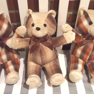 May include: Three plush teddy bears made from brown, tan, and white plaid fabric. Each bear features a cream-colored face, dark button eyes, a stitched nose, and a dark brown ribbon tied around its neck. The paws and feet are made of cream fabric.