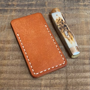 May include: A brown leather pocket knife case with white stitching. The case is empty and has a smooth, textured surface.