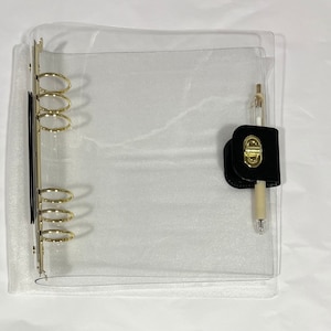 May include: A clear plastic binder with gold rings and a black leather pen holder with a gold clasp. The pen holder has a pen inside.