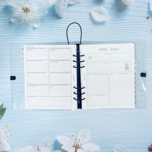 May include: A white planner with a clear plastic cover. The planner is open to the April 2024 calendar page. The calendar page has a section for appointments, reminders, and notes. The planner also has a reflection section with prompts for self-reflection.