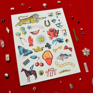 May include: A white print with a colorful collection of vintage tattoo flash designs. The print features a tiger, a rose, a horseshoe, a sun, a butterfly, a crown, a heart, a fish, a key, a domino, a cherry, a horse, a seashell, and the number 777.