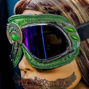 Pu&ograve; includere: Occhiali protettivi verdi con lenti scure riflettenti e una fascia elastica nera. La montatura &egrave; decorata con intricati ricami verdi, piccole perline verdi e un ornamento in filigrana metallica con una pietra verde liscia e ovale.