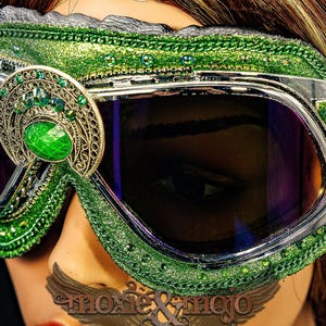 Pu&ograve; includere: Occhiali protettivi verdi con montatura in argento metallizzato e lenti scure. La montatura &egrave; decorata con glitter verdi, piccole perline verdi e un ornamento centrale in filigrana con un grande cabochon verde. Accenti a forma di foglia.