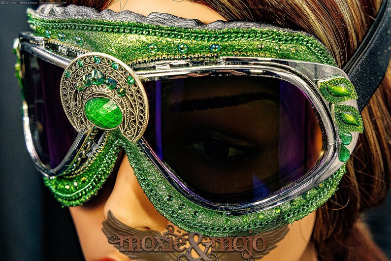Pu&ograve; includere: Occhiali protettivi verdi con montatura in argento metallizzato e lenti scure. La montatura &egrave; decorata con glitter verdi, piccole perline verdi e un ornamento centrale in filigrana con un grande cabochon verde. Accenti a forma di foglia.