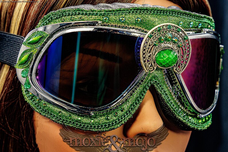 Pu&ograve; includere: Occhiali protettivi verdi con lenti scure e montatura argentata. L'esterno &egrave; decorato con glitter verdi, piccoli strass verdi e un vistoso ornamento in filigrana color argento antico con una grande pietra preziosa ovale di colore verde.